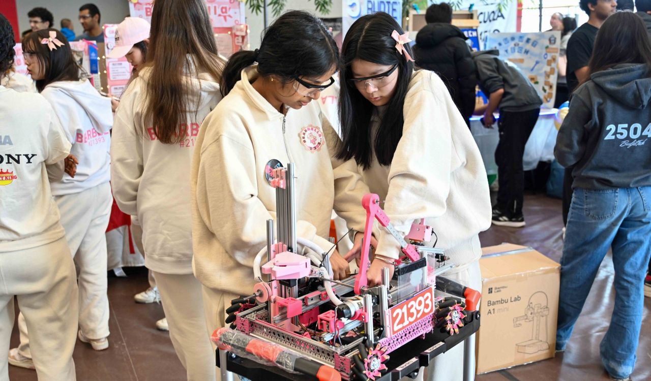 Two teenage girls work on a robot at a robotics competition.