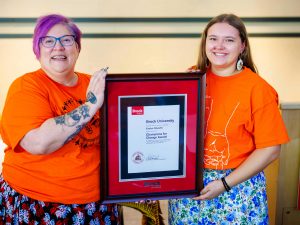 Two women stand side-by-side and hold a framed certificate.
