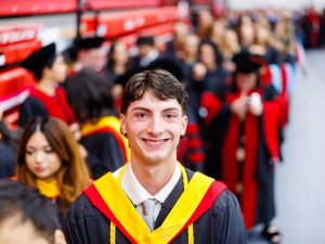 Man wearing academic regalia smiles in front of a group of graduates at Brock University's 118th Convocation.