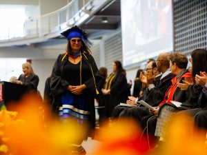 Woman wearing academic regalia walks across a stage during Brock University's 118th Convocation.