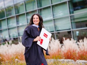 Woman wearing academic regalia smiles while holding degree in a portfolio during Brock University's 118th Convocation.