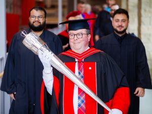 Men wearing academic regalia walk down a ramp during Brock University's 118th Convocation.