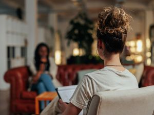 Close-up view of the back of a therapist's head, with a patient, who is out of focus, sitting across from her on a couch.