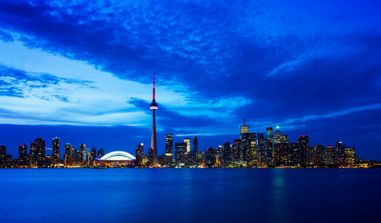 The Toronto skyline at dawn or dusk showing the CN Towers and Rogers Centre.