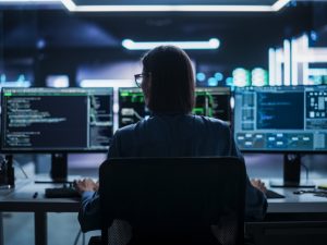 Silhouette of a woman sitting in front of several computer screens in a darkened room.
