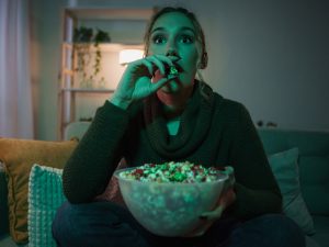 A woman, who looks startled, eats popcorn while watching television.