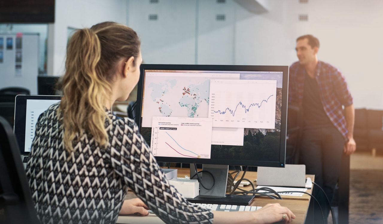 A woman works on a map on a computer with a man standing in the background.