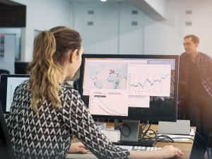 A woman works on a map on a computer with a man standing in the background.