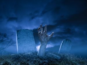 A zombie or monster hand pushing through the dirt at grave site in a graveyard on a dark Halloween night.