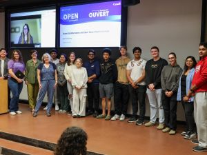Ada Oliver (on screen), Junearn Lenon and Cara Scarfone of the Treasury Board of Canada Secretariat stand on stage with Brock’s Manager, Privacy & Records Management Marion Hansen, Associate Professor Karen Louise Smith and several COMM 3P19 students
