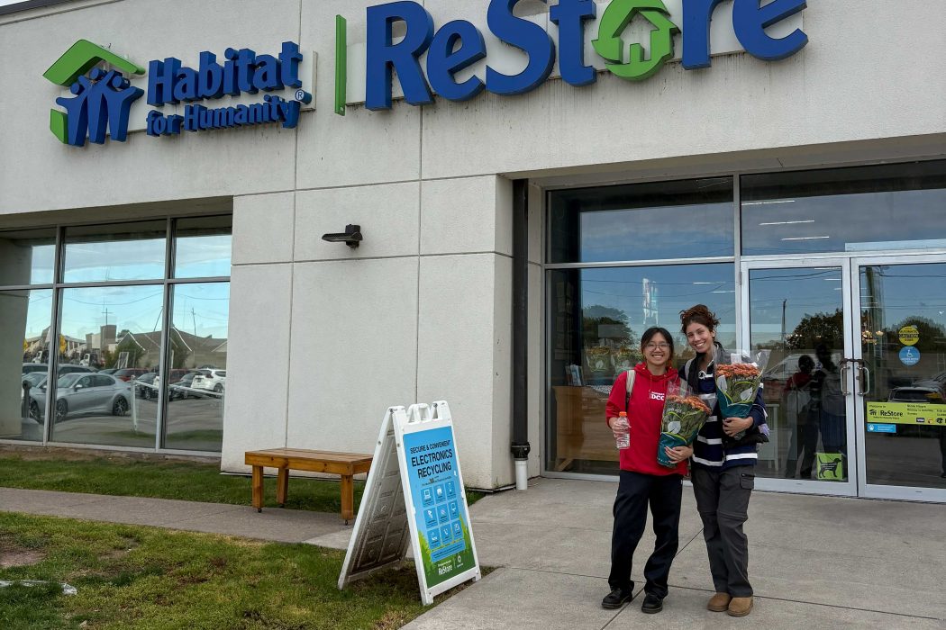 Two young women pose in front of a Habitat for Humanity store.