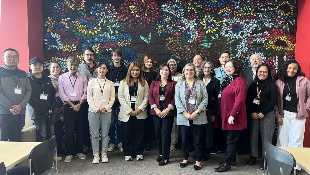 A large group of people pose for a photo in front of a colourful mural of flowers.