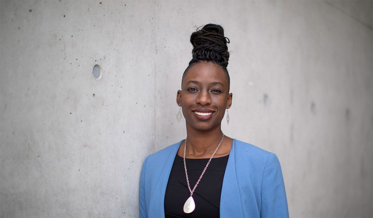 A woman wearing a blue blazer poses against a grey wall.