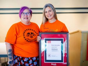Two women stand side-by-side and hold a framed certificate