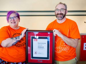 A man and a women stand side-by-side and hold a framed certificate.