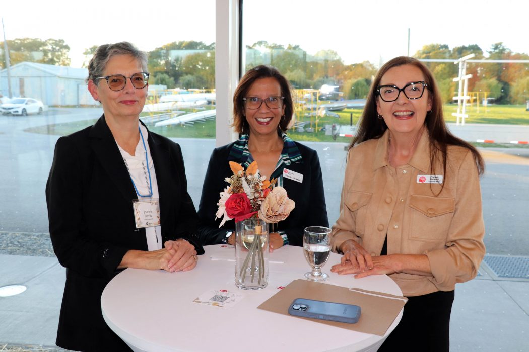 Three women stand at a table at an event. 