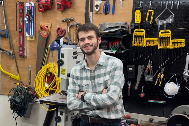 A man stands in front of a wall of tools in a garage. 