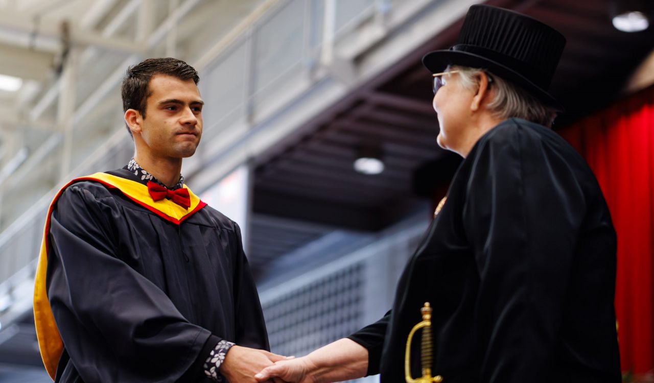 Man wearing black graduation gown shakes hands with a member of the stage party during Brock’s 118th Convocation.