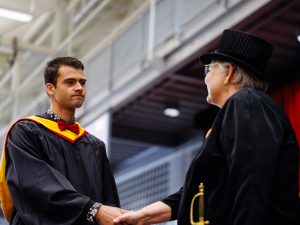 Man wearing black graduation gown shakes hands with a member of the stage party during Brock’s 118th Convocation.