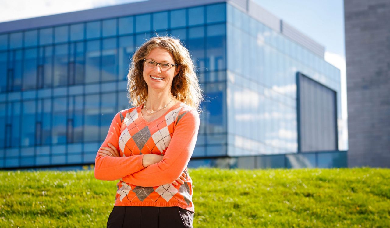 A woman poses outside with a glass building in the background.