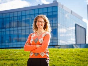 A woman poses outside with a glass building in the background.