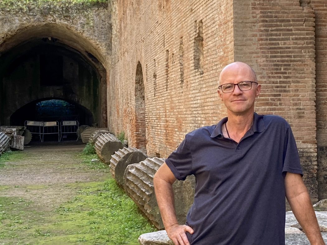 A man stands outdoors in ancient ruins in Italy.