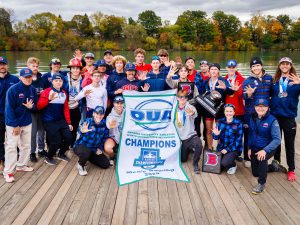 A group of men holding an OUA champions banner stand on a dock with a waterway behind them.