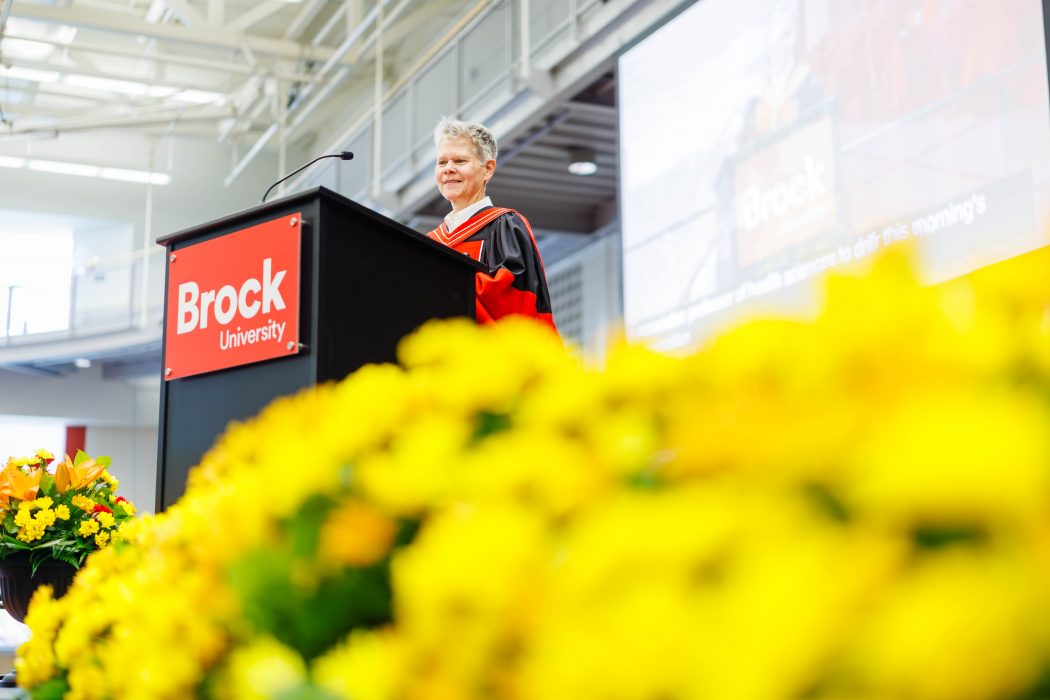 Professor wearing a black graduation gown stands at a podium to deliver a speech during Brock University's 118th Convocation.