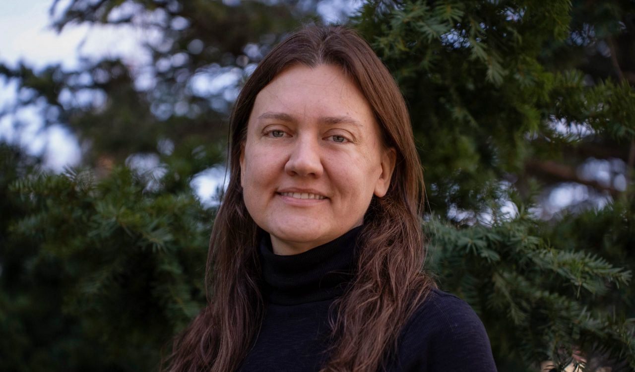 A woman in a black shirt poses for a photo in front of a tree outside.