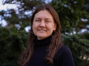 A woman in a black shirt poses for a photo in front of a tree outside.