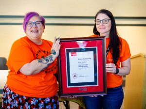 Two women stand side-by-side and hold a framed certificate.