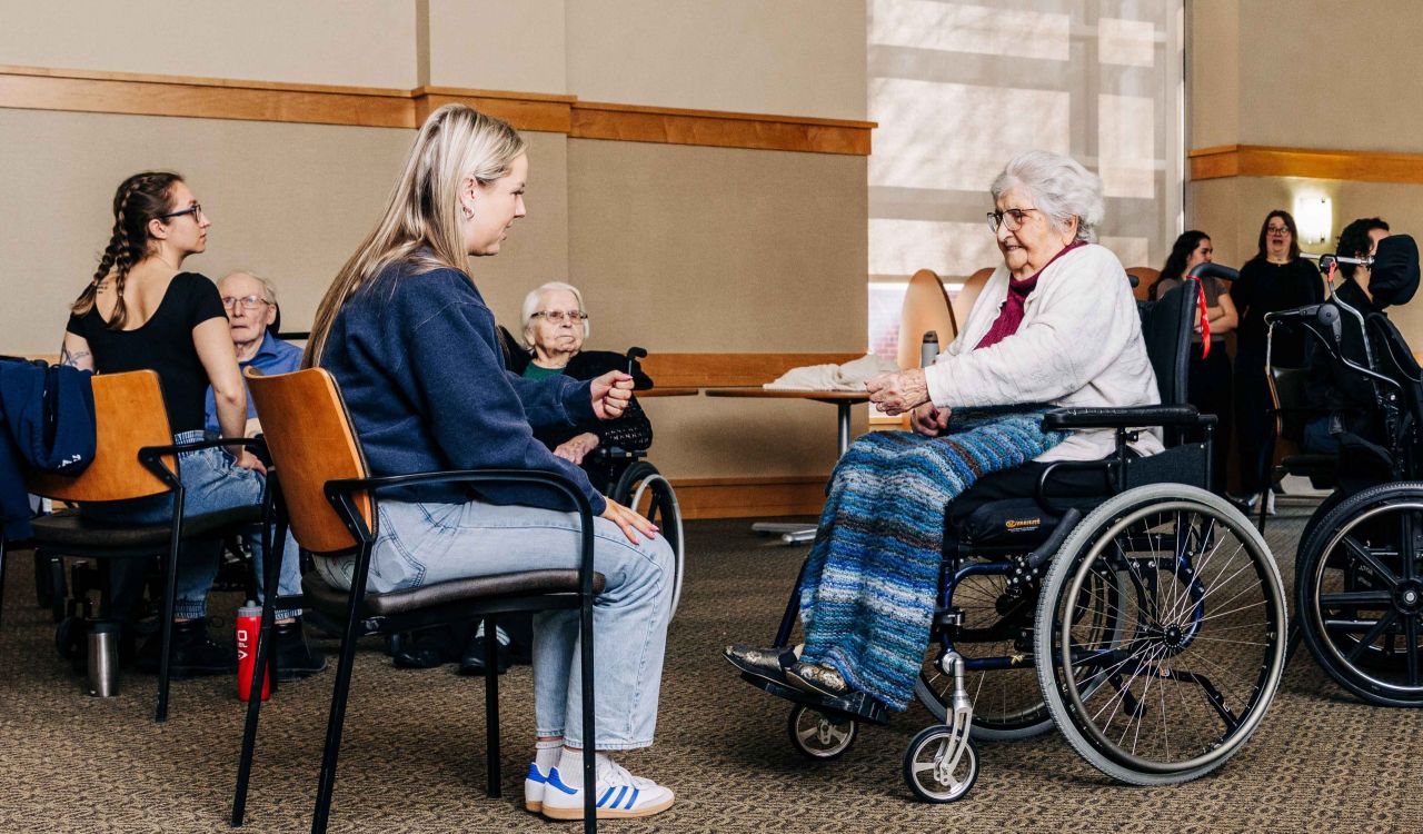 A university student speaks to an elderly woman who is using a wheelchair.
