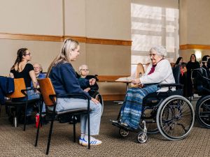A university student speaks to an elderly woman who is using a wheelchair.