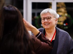 A woman with short gray hair smiles while talking to another guest.