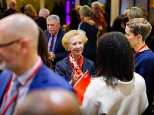 Guests mingle at a reception, with a woman in an orange scarf smiling in conversation.