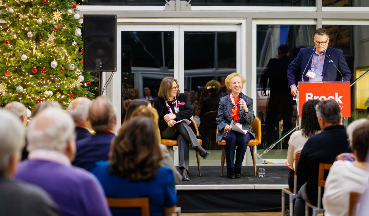 A panel speaks on stage beside a decorated Christmas tree at Brock University.