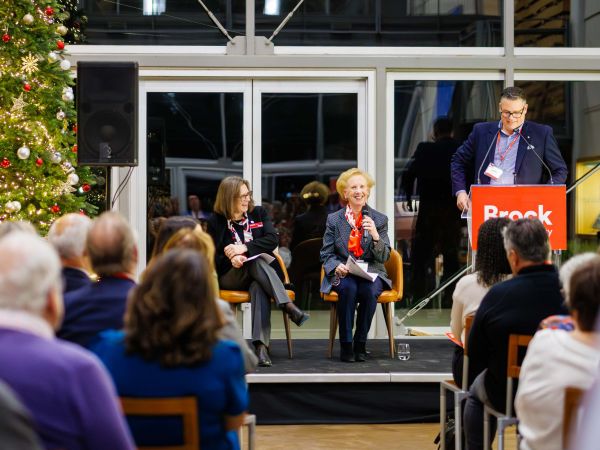 A panel speaks on stage beside a decorated Christmas tree at Brock University.