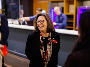 A woman with glasses laughs while talking with other guests at the reception.