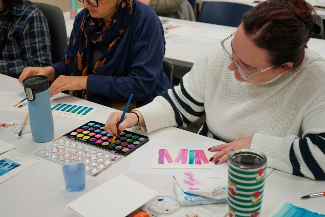 A woman paints a picture of candles using watercolour paints.