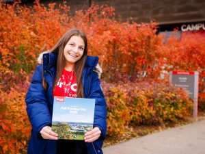 A woman stands outside in front of bright orange fall leaves.