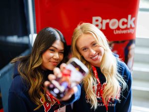 Two students take a cheerful selfie at a Brock University booth.