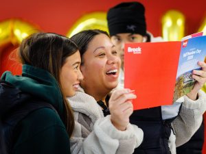 Two smiling visitors look at a Fall Preview Day 2025 brochure together.