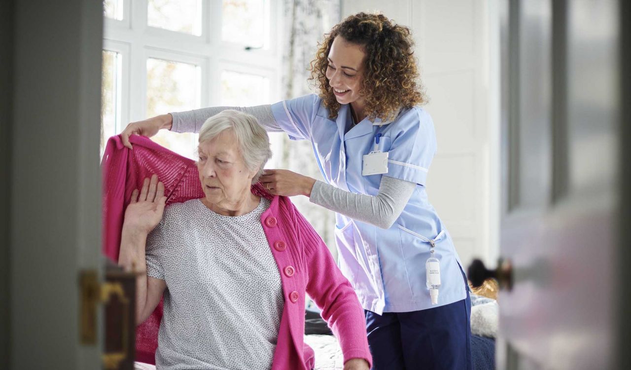 A health-care worker helps an elderly woman put on a sweater.