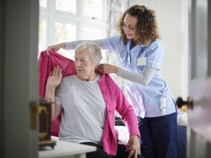 A health-care worker helps an elderly woman put on a sweater.