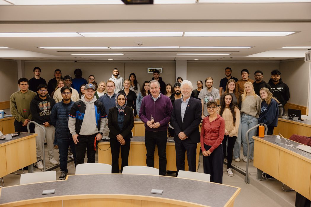 People in a classroom stand in a group, with one man holding a glass award.