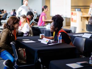 Two women chat at a table during an event.