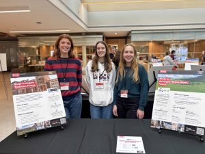 Three people stand behind a table at an information fair.