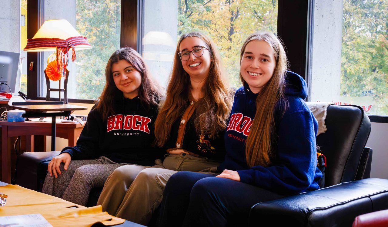 Three women sit next to one another on a couch.
