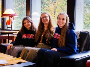 Three women sit next to one another on a couch.