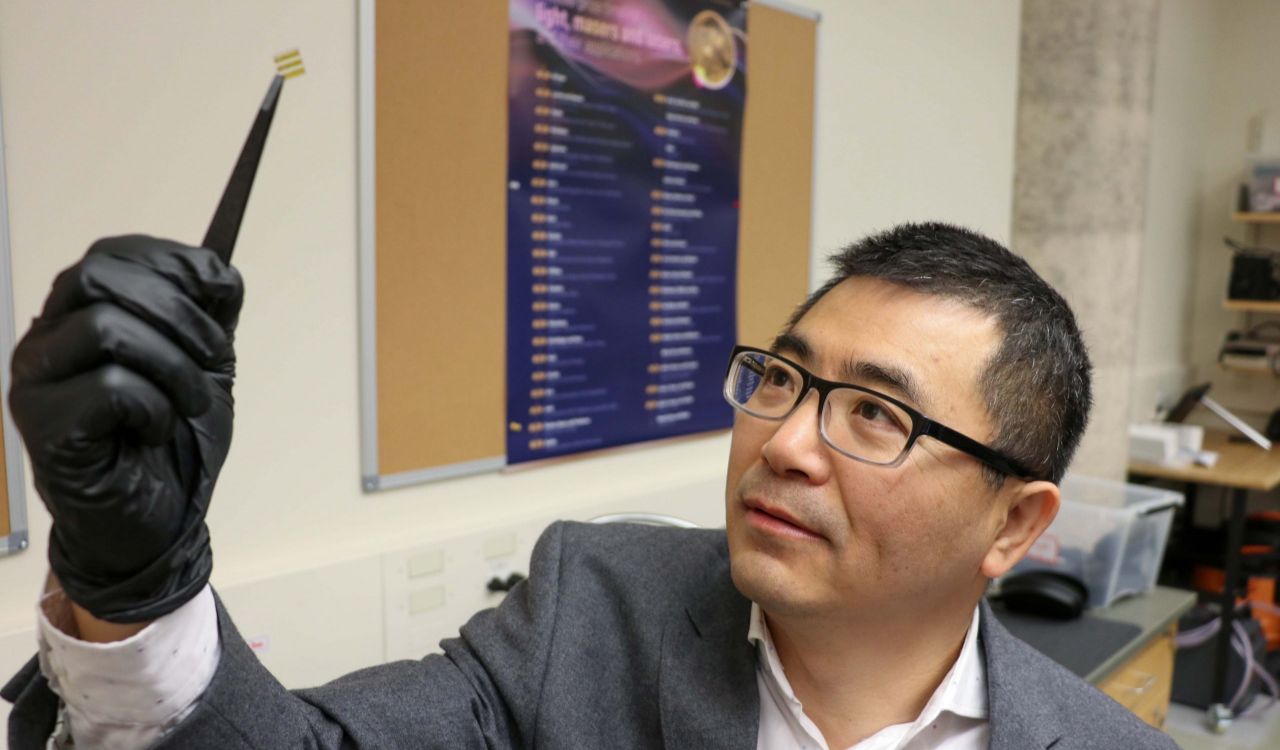 A man holds up a tiny chip in a university lab.